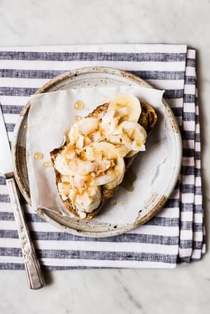 Almond Butter Toast with Bananas, Toasted Coconut, sea salt and honey on a plate with a striped linen.
