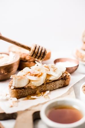 honey being drizzled on Almond Butter Toast with Bananas and Toasted Coconut