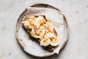 Almond Butter Toast with Bananas, Toasted Coconut flakes, honey and flakey salt on parchment paper on a plate