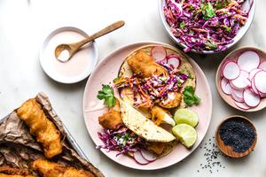 Beer-Battered Fish Tacos with sesame slaw and a spicy cream on a plate with radishes and cilantro