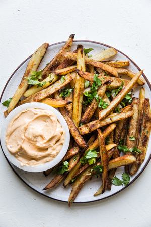 baked French fries on a plate with cilantro and chipotle aioli and cilantro