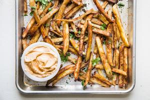 baked French fries on a baking sheet with cilantro and chipotle aioli
