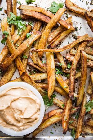baked French fries on a baking sheet with cilantro and chipotle aioli