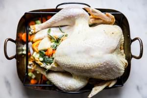 raw dry brined turkey stuffed with herbs and oranges in a roasting pan with vegetables