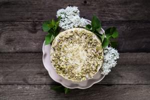 Yogurt and Olive Oil Pistachio Cake With Lemon Buttercream on a cake stand with flowers