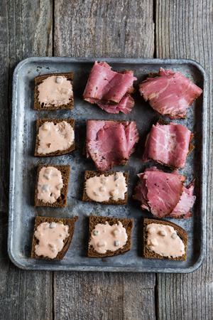 small slices of rye bread on a baking sheet topped with Russian dressing pastrami