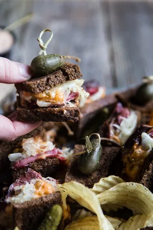 Rueben sliders on a baking sheet made with rye bread, Russian dressing, sauerkraut and provolone topped with pickles