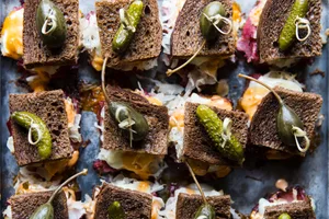 Rueben sliders on a baking sheet made with rye bread, Russian dressing, sauerkraut and provolone topped with pickles