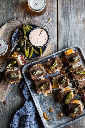 Rueben sliders on a baking sheet made with rye bread, Russian dressing, sauerkraut and provolone topped with pickles