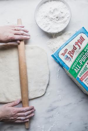 2 hands rolling out dough on a floured surface for Cardamom Rolls with Almond Glaze