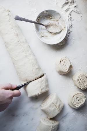hands cutting Cardamom Rolls with Almond Glaze