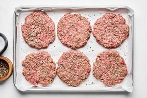 raw burger patties on a parchment lined baking sheet ready for cooking
