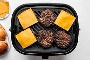 Cheeseburgers sizzling on a grill with grill marks and topped with melting american cheese slices
