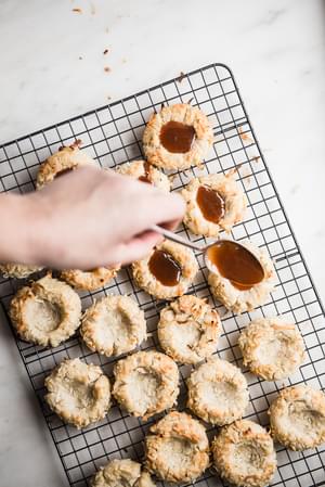 caramel being poured onto Coconut Thumbprint Cookies with Salted Caramel sauce
