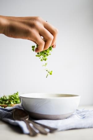 hand dropping micro greens on a bowl of Corn and Leek Bisque