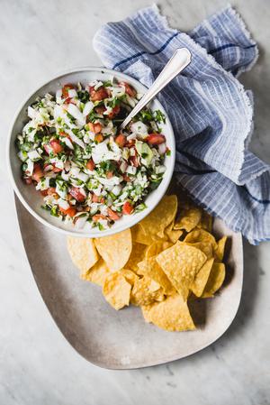 Pico De Gallo with Cabbage in a bowl with tortilla chips on a plater with a linen
