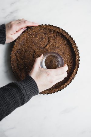 2 hands pressing chocolate graham cracker crust into a pie pan