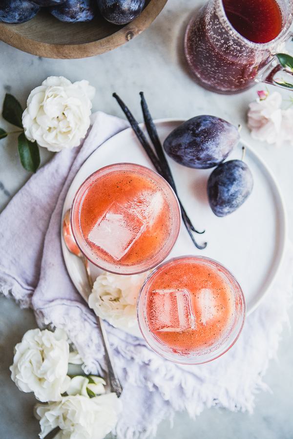 2 cups of Plum Shrub with vanilla bean and fresh plums on a plate