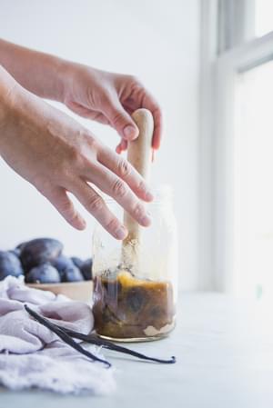 two hands muddling sugar and plums in a pitcher for Vanilla Plum Shrub