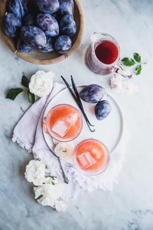 2 cups of Vanilla Plum Shrub with vanilla bean and fresh plums on a plate