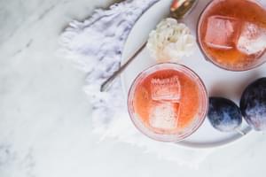 2 cups of Vanilla Plum Shrub with vanilla bean and fresh plums on a plate