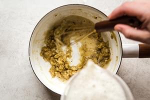 hands pouring a whisking beer into a small bot with roux base