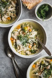 White Bean Chicken soup in a bowl with carrots fresh dill, chard, carrots and celery with a spoon.