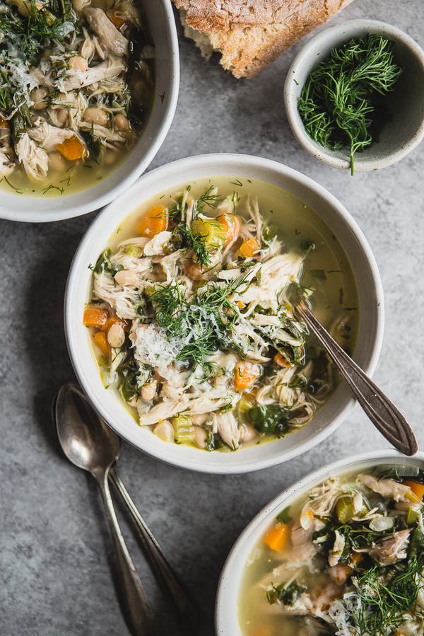 White Bean Chicken soup in a bowl with carrots fresh dill, chard, carrots and celery with a spoon.