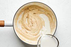 milk being poured into a pan with a flour and butter rue