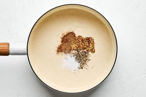 whole grain mustard, salt, pepper, and nutmeg being stirred into a butter, flour and milk rue in a pan