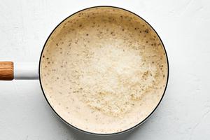 Parmesan being stirred into a cream sauce in a pan