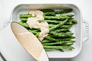 cream sauce being poured over blanched asparagus in a casserole dish
