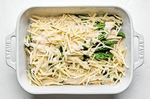 Gruyère cheese sprinkled on top of asparagus and cream sauce in a baking dish