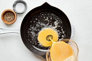 whisked eggs with salt and pepper being poured into a skillet with melted butter to make an omelette