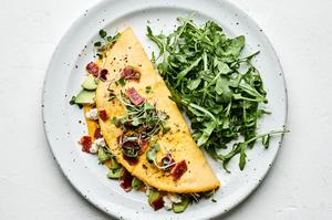 an omelette filled with avocado, goat cheese and bacon topped with micro greens and more crumbled bacon