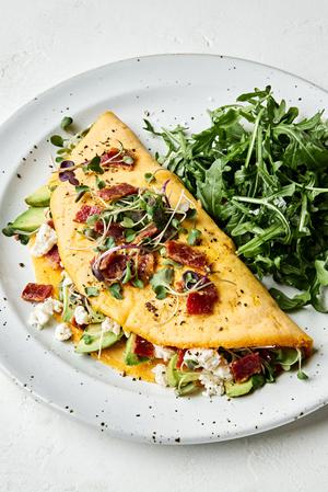 an omelette filled with avocado, goat cheese and bacon topped with micro greens and more crumbled bacon