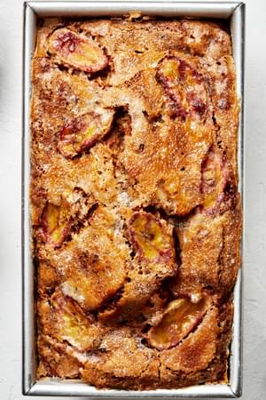 homemade banana bread topped with thinly sliced bananas and sprinkled with sugar in a loaf pan just out of the oven