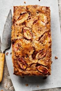 homemade banana bread topped with thinly sliced bananas and sprinkled with sugar sitting on a cutting board with a knife