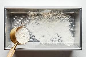 a loaf pan being prepared with butter and flour to bake homemade banana bread