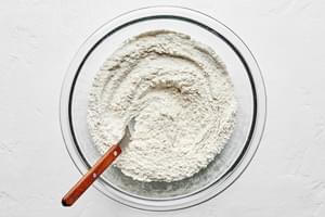 flour, baking soda and salt being whisked together in a mixing bowl