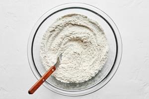 flour, baking soda and salt being whisked together in a mixing bowl