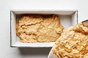 banana bread dough being poured into a loaf pan that has been prepared with butter and flour