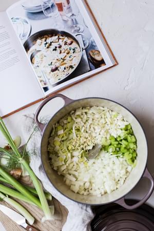 Leeks, fennel, onion and celery chopped in soup pot for bourride soup next to a cookbook