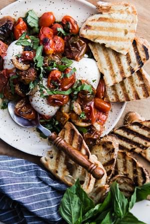 Braised Tomatoes with Burrata, basil and grilled bread on a plate