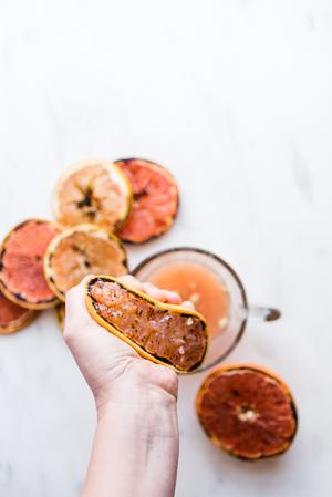 hand squeezing a charred grapefruit juice into a measuring cup