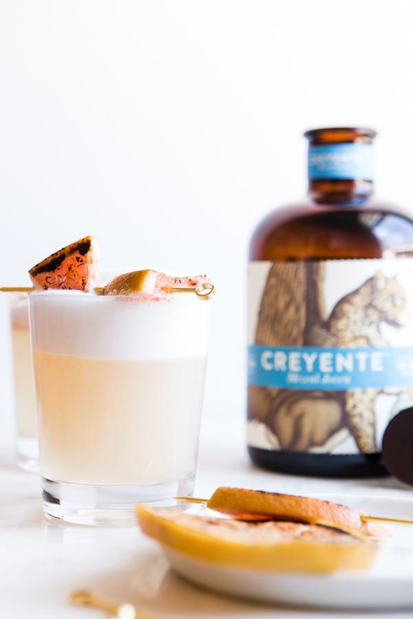 A foamy mezcal Paloma sour with charred grapefruit on the rim