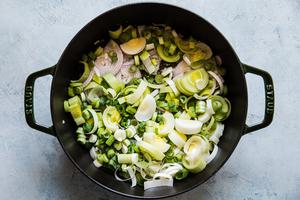 shallots, leeks, green onions and yellow onions being cooked in a pan with butter