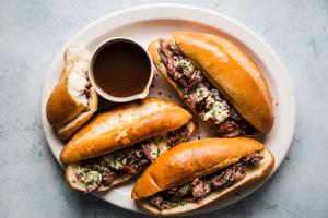 the best french dip sandwiches on a serving plater with thinly sliced steak, garlic butter, swiss cheese and au jus sauce