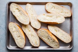 Buttered hoggie rolls with garlic powder on a rimmed baking sheet