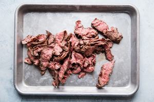 thin slices of flank steak on a baking sheet
